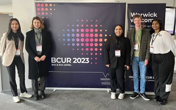 Photo of BCUR23 students in front of logo